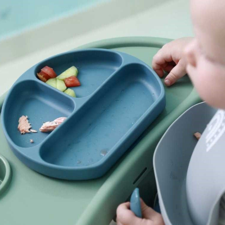 Baby With Silicone Bib Eating From Silicone Plate With Spoon On Highchair