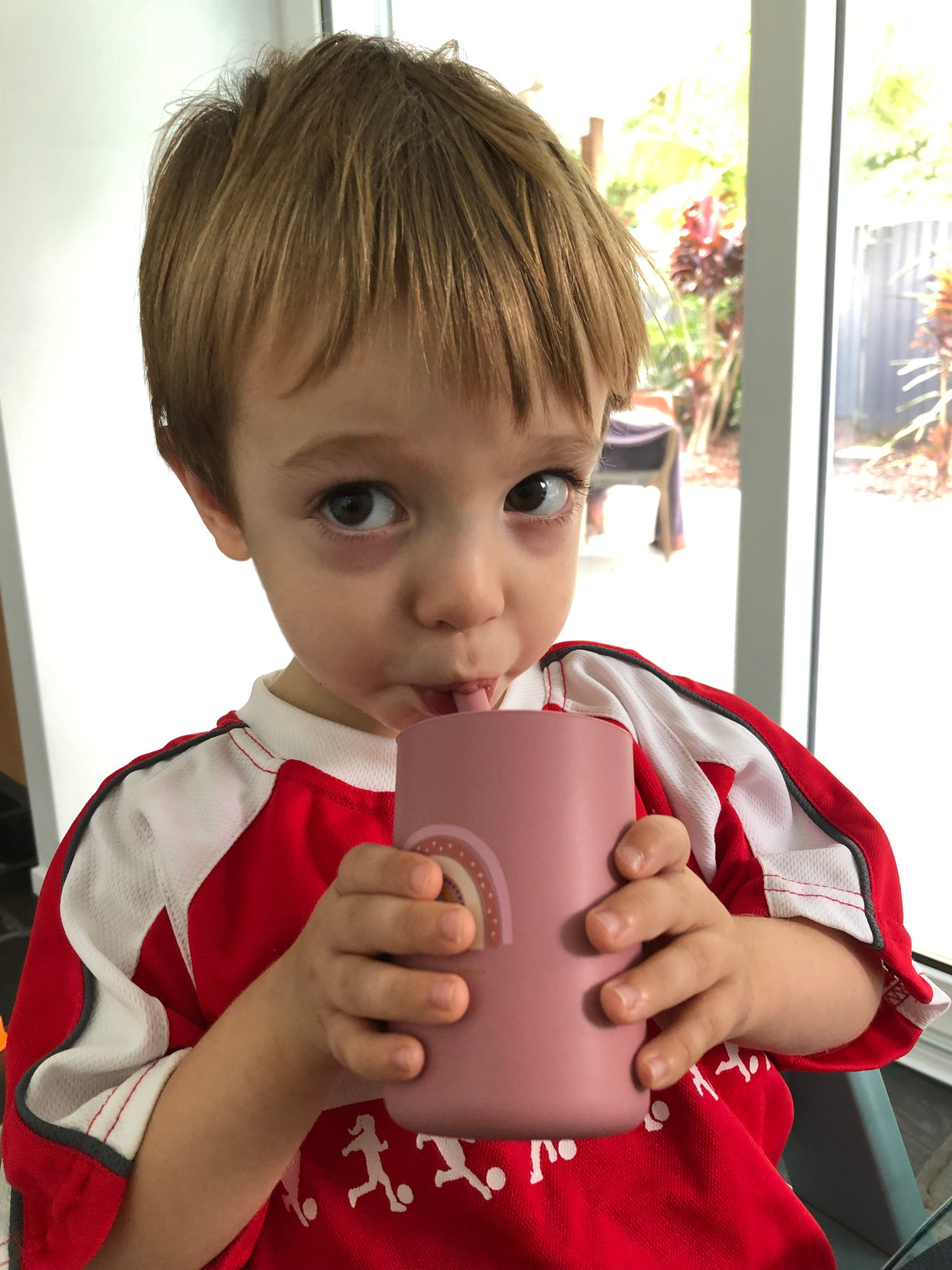 Toddler drinking from rainbow rose tall straw silicone cup